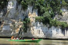 Wisata susur sungai di Kampung Merasa dengan pemandangan bukit karst dan tumbuhan hijau di atasnya.