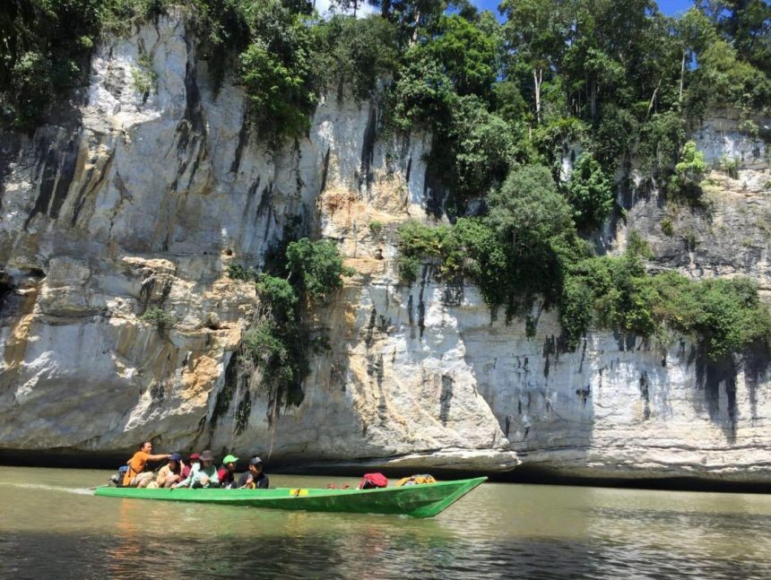Wisata susur sungai di Kampung Merasa dengan pemandangan bukit karst dan tumbuhan hijau di atasnya.