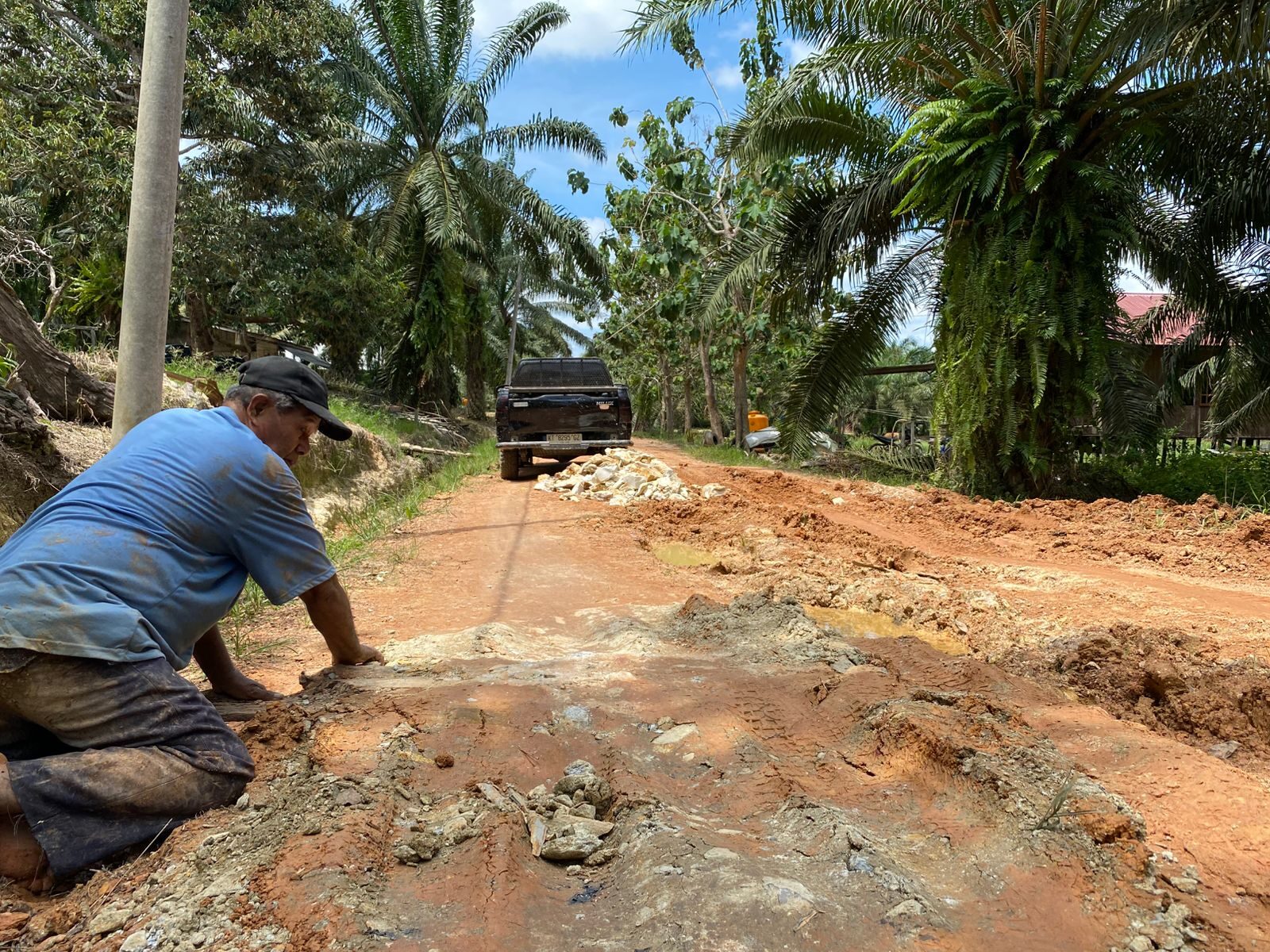Alimuddin menyebar batu gunung untuk dijadikan fondasi jalan di Jalan Rusa, Kampung Harapan Jaya, Kecamatan Segah, Minggu (20/7/2025). (Sulaiman/BT)