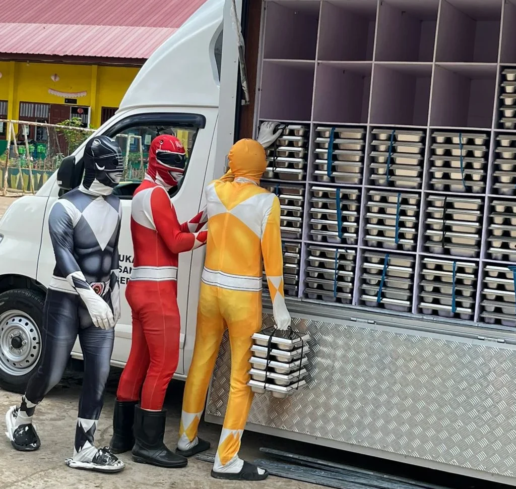 Petugas SPPG di Sei Bedungun berpakaian Power Ranger mengantarkan MBG untuk siswa.