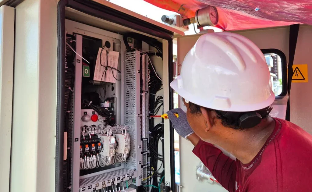 Pekerja sedang melakukan pekerjaan wiring cable pada panel kontrol listrik dengan memastikan setiap koneksi kabel terpasang sesuai standar instalasi dan prosedur keselamatan kerja